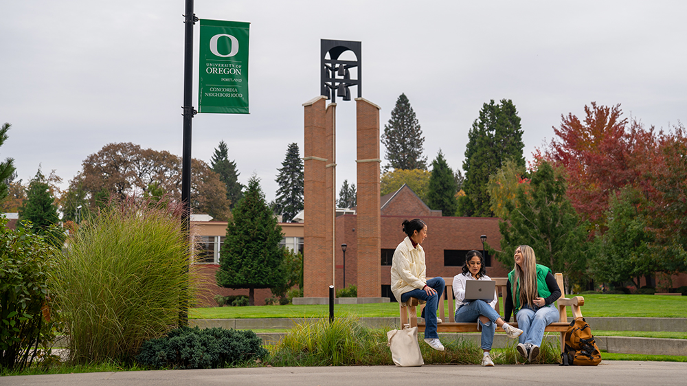 Three students sitting on a bench and talking at the UO Portland Campus