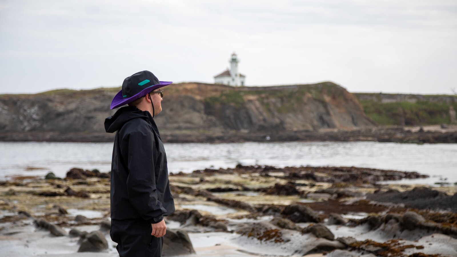 A student walks across rocky tide pools near a lighthouse.