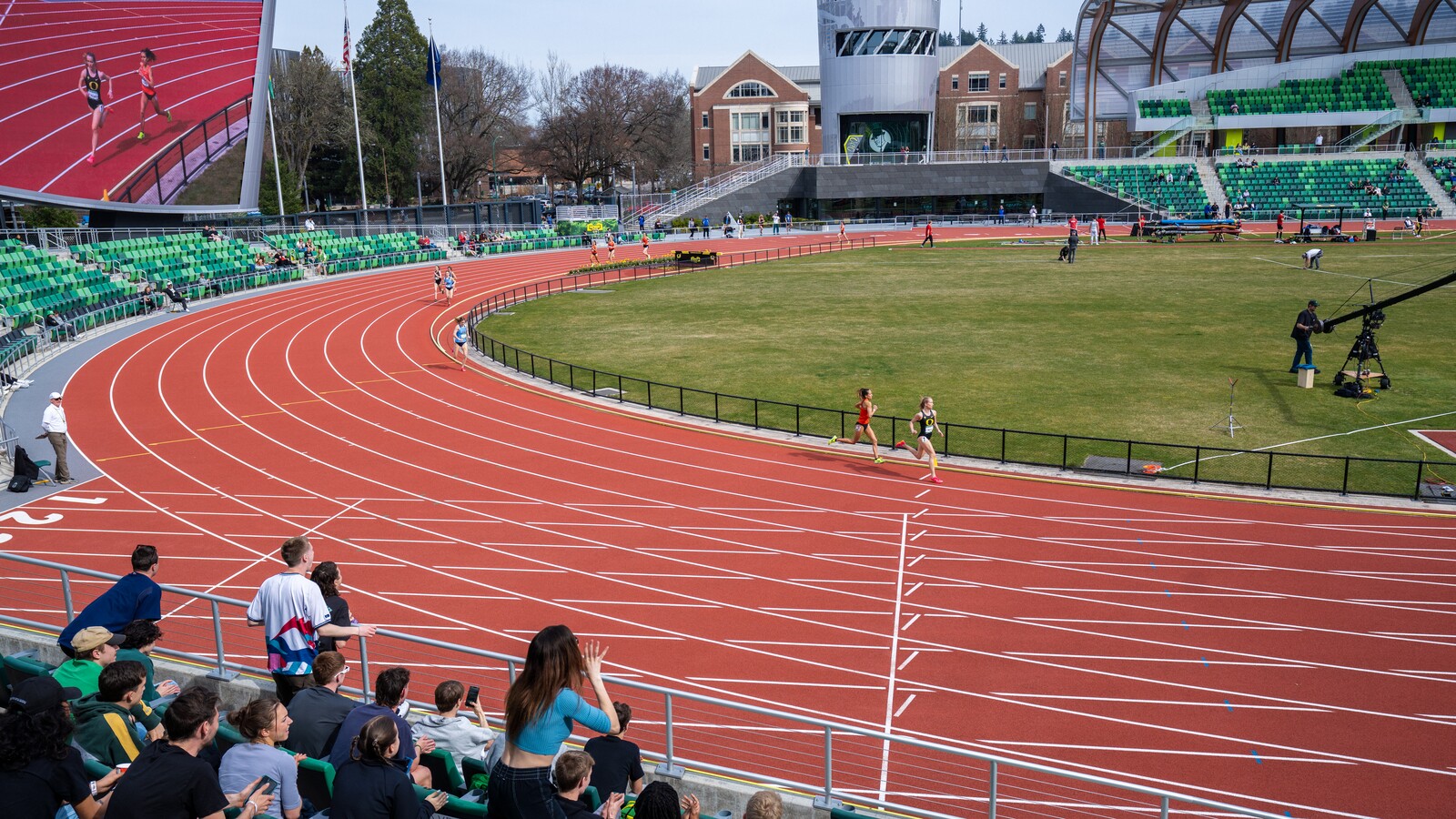 Runners race around Hayward Field as spectators cheer from trackside seats.
