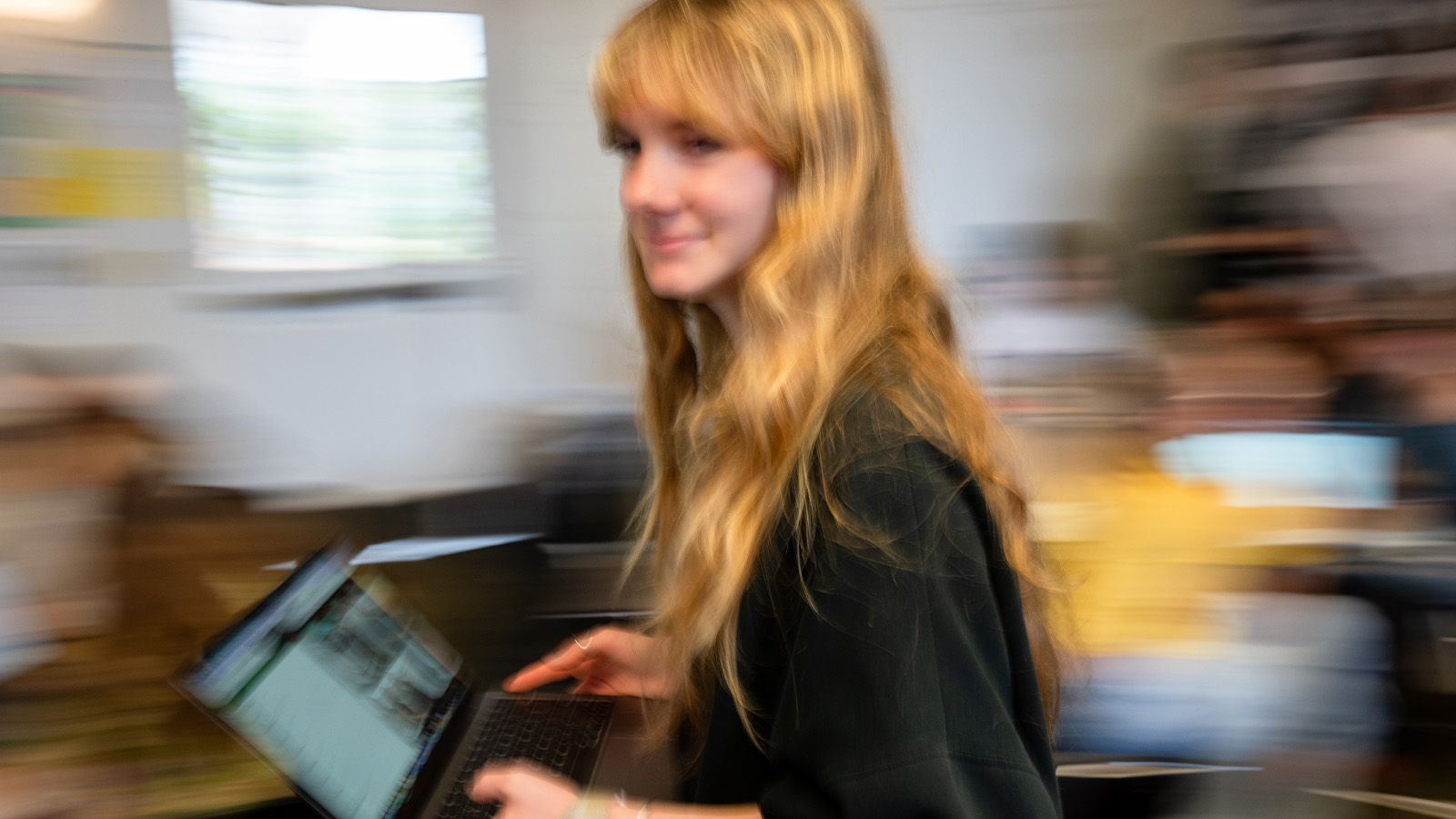 student walking across classroom holding laptop