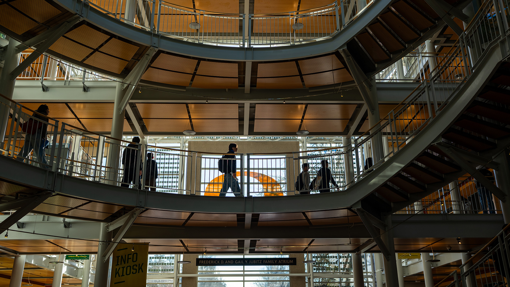 Students walk a walkway in a multi-story campus atrium.