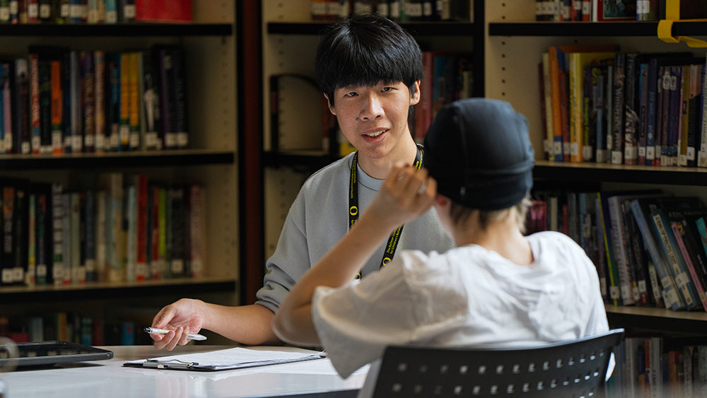 A UO student speaking with a teenager at a table