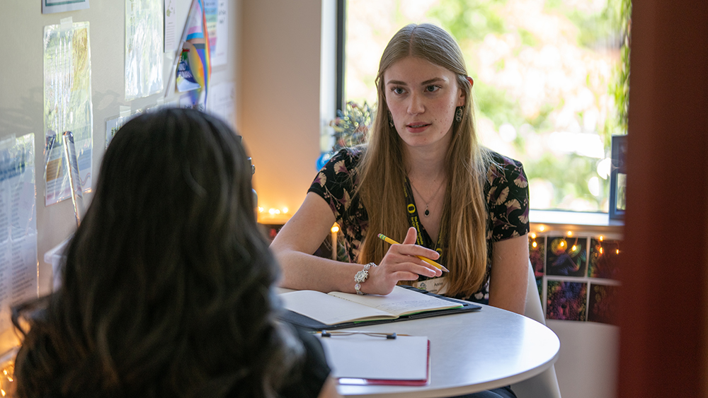 A UO student talking to a teenager at a desk