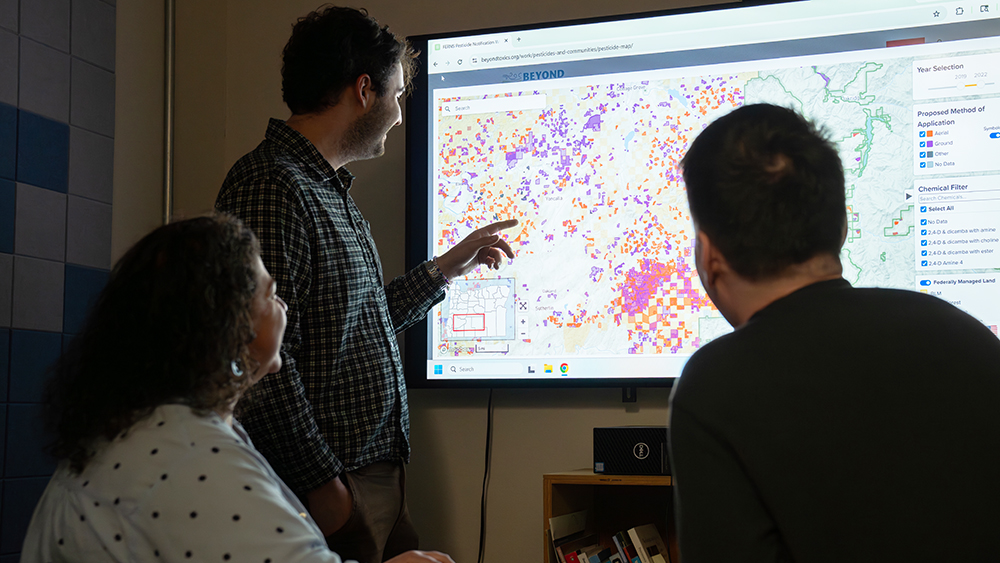 Two students looking at a data map that a professor is pointing to.