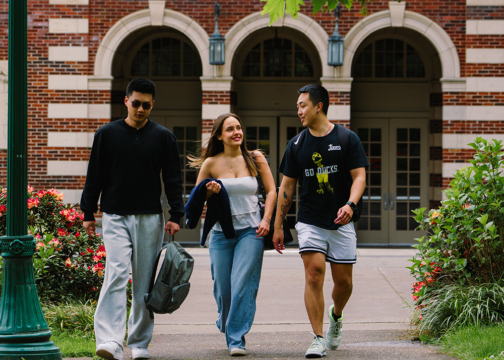 Three students talking and walking outside a building on the UO campus