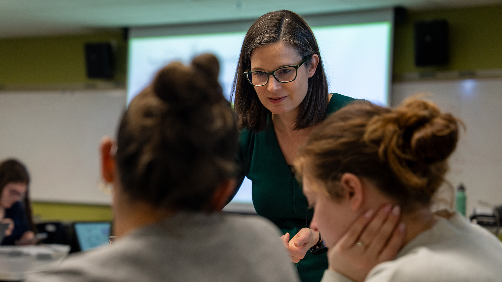 An instructor talks with students around a classroom table.