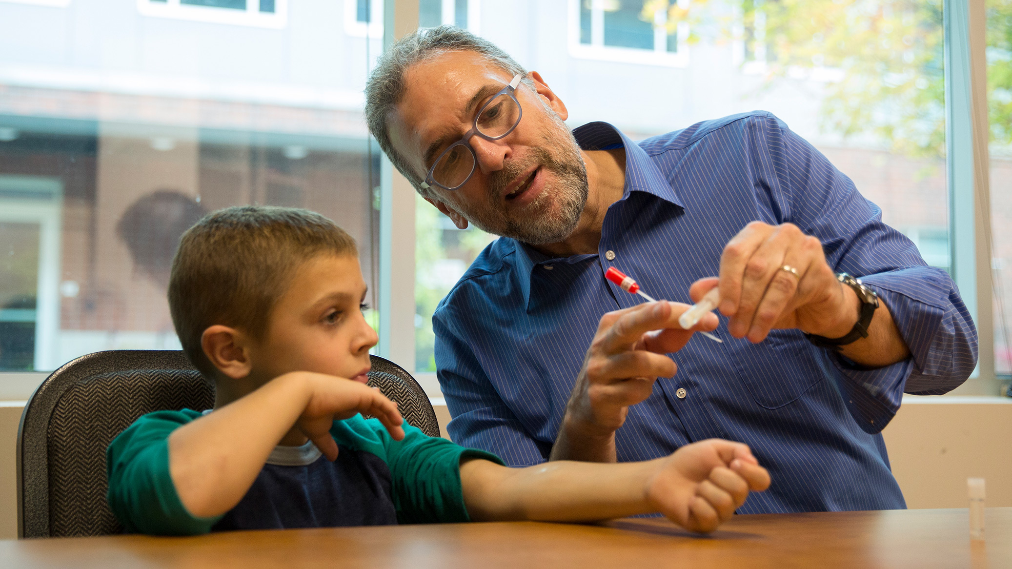 An adult shows a child a swab at a table.