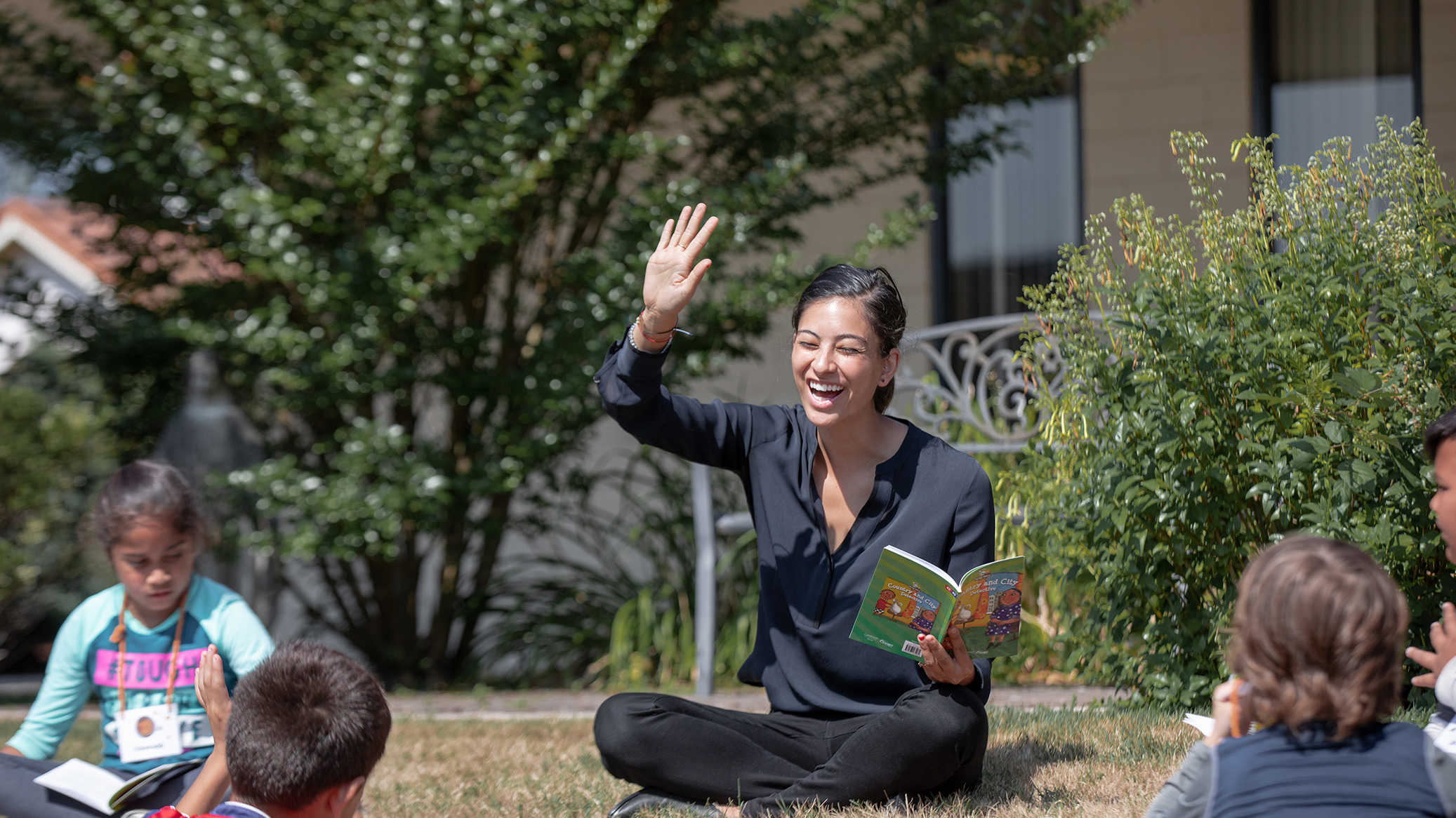 A teacher reads to children sitting on the grass.
