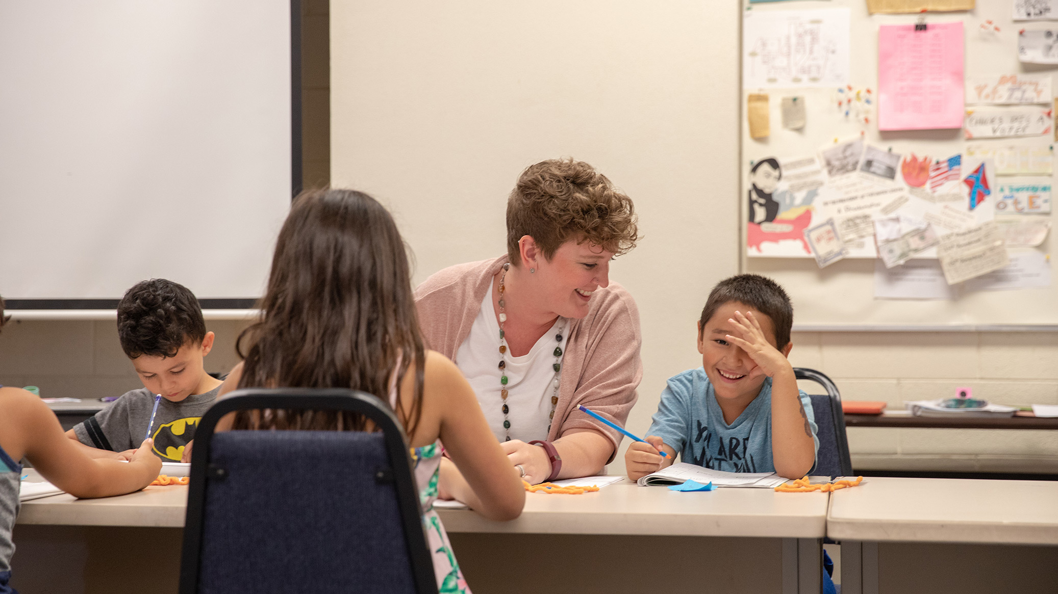 A teacher smiles with children writing at a table.