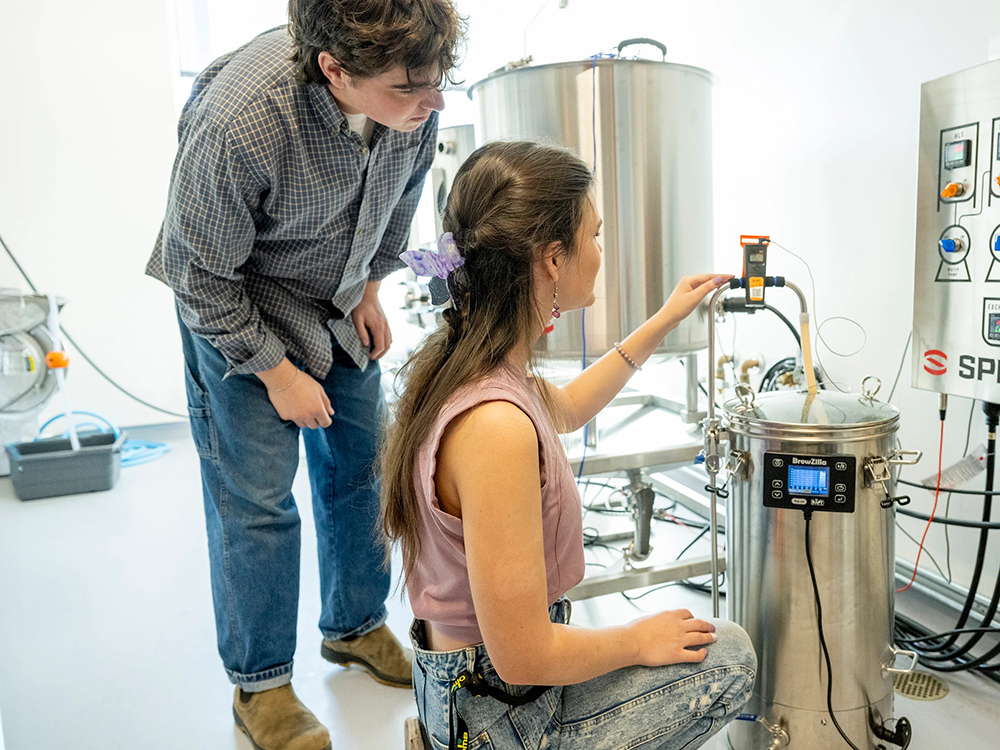 Two students standing next to a brewing vessel