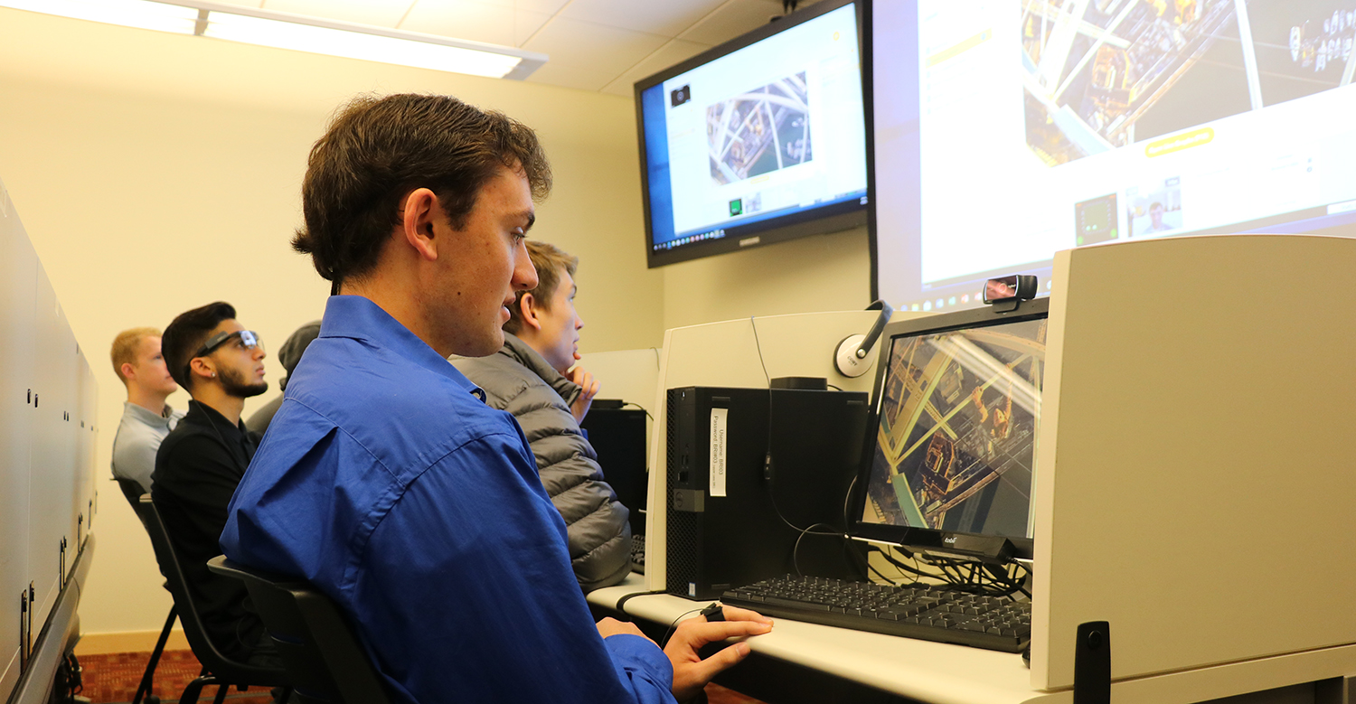 Student working on a computrer in front of a large screen