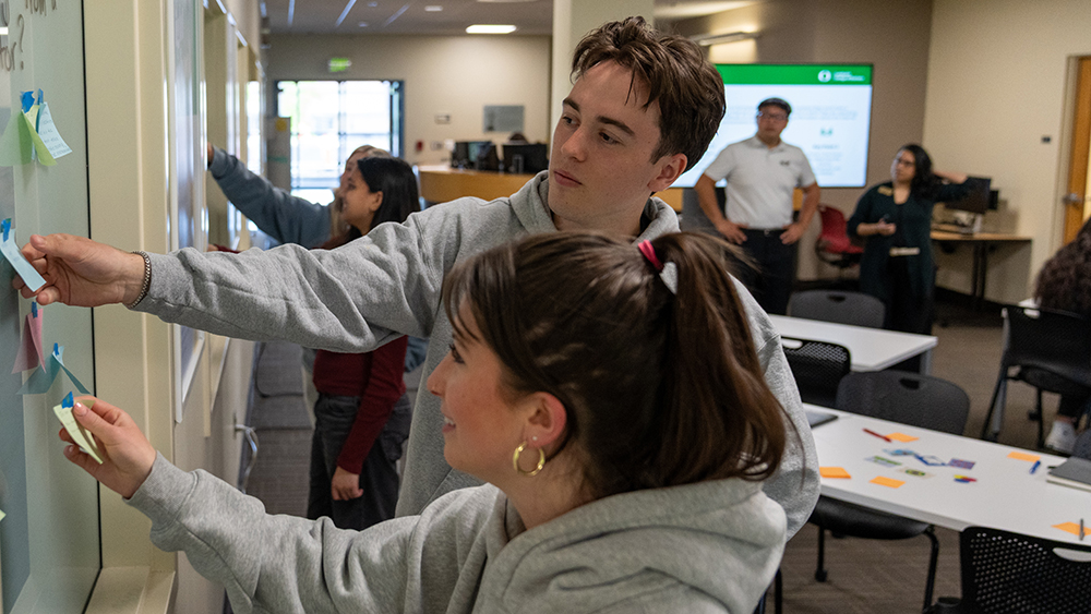 Two students arranging sticky notes on a whiteboard