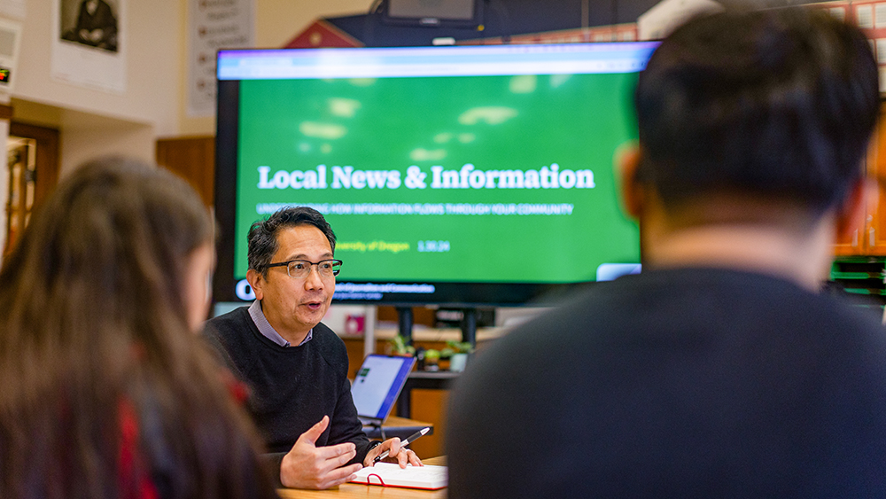 Faculty member talking with students at a table