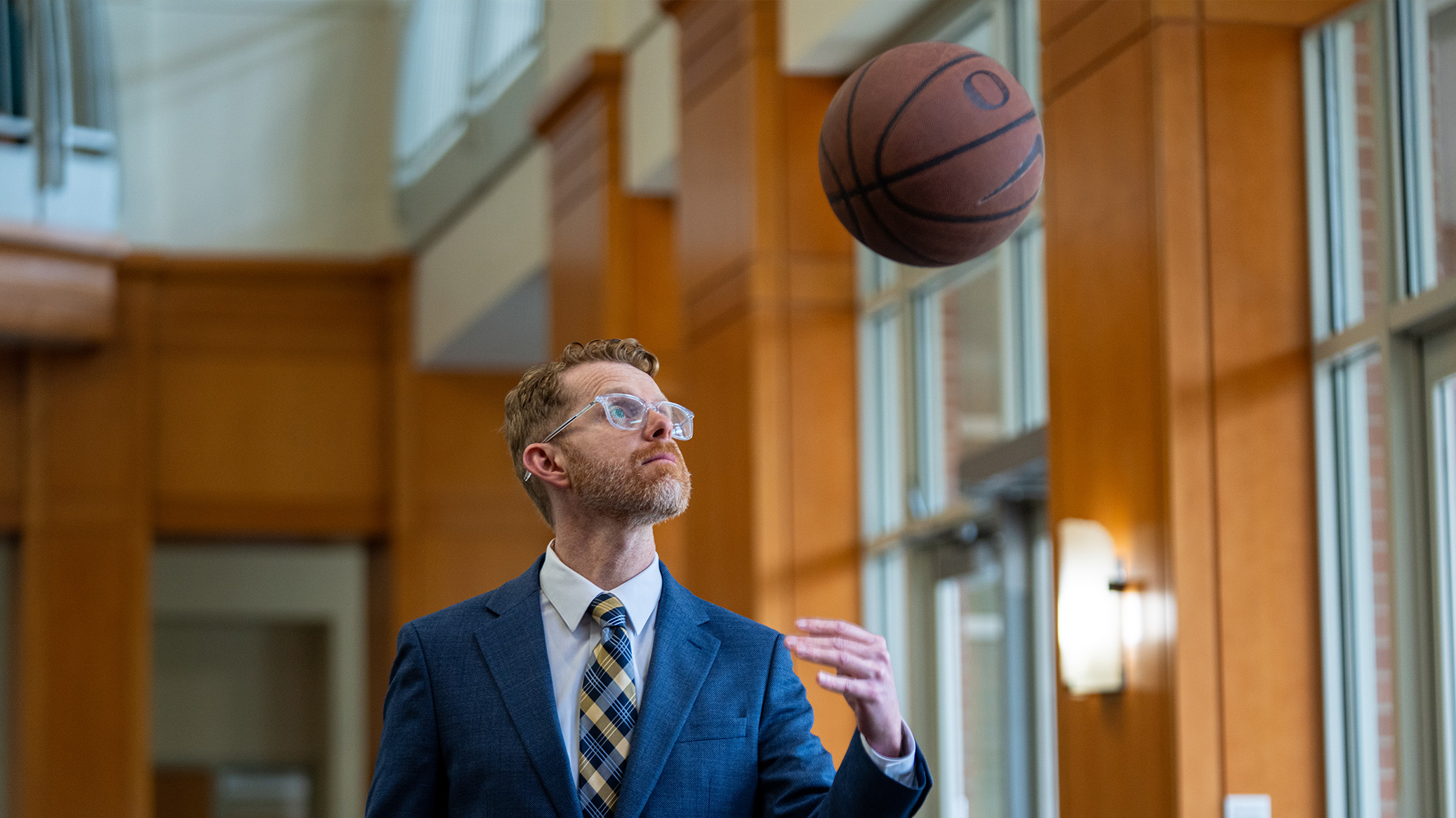 A man in a suit tossing a basketball in a hallway