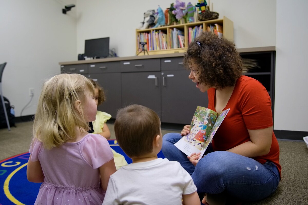 A clinician reads a story to children seated on a classroom rug.