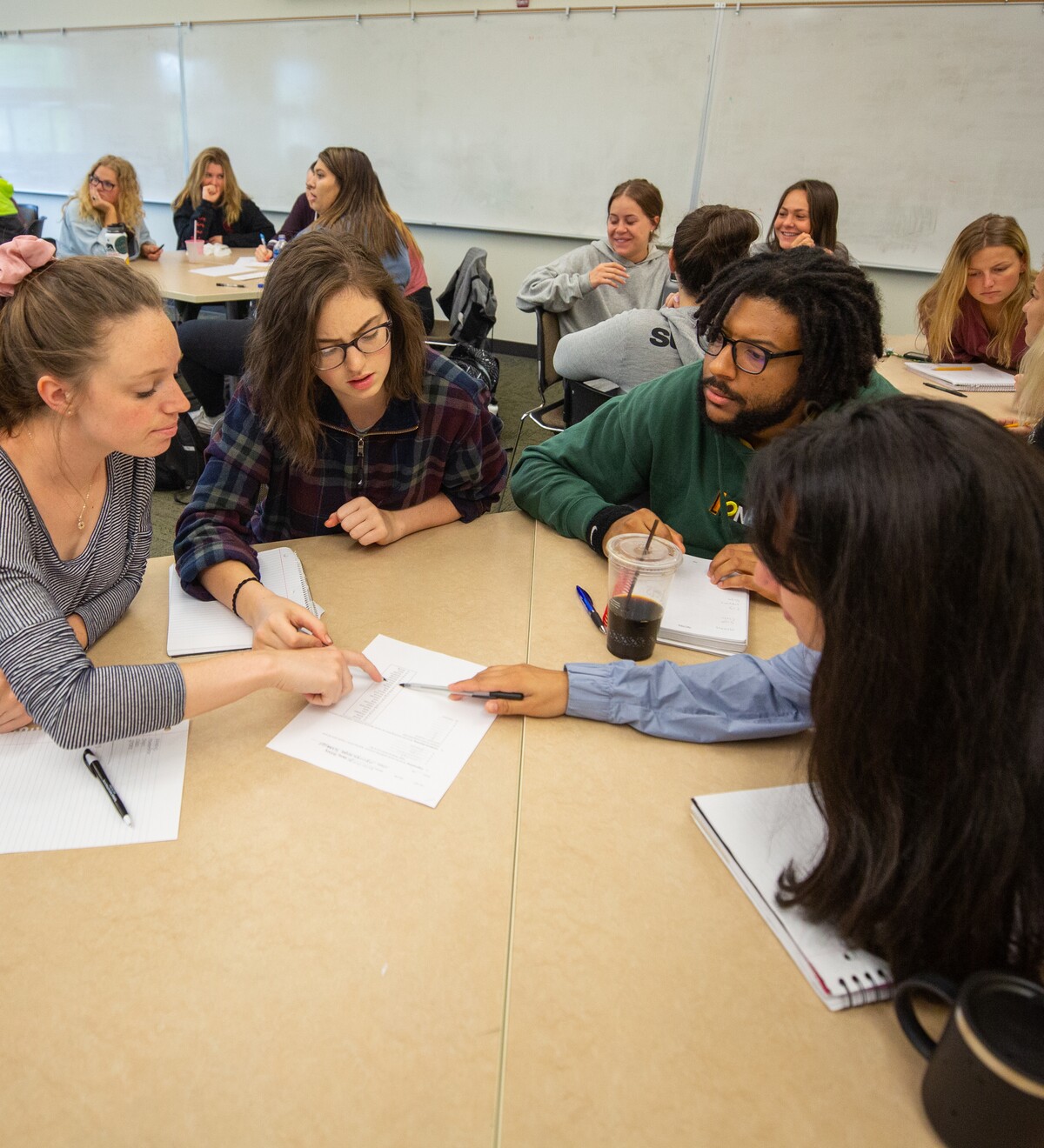 Students discuss class materials around a table.