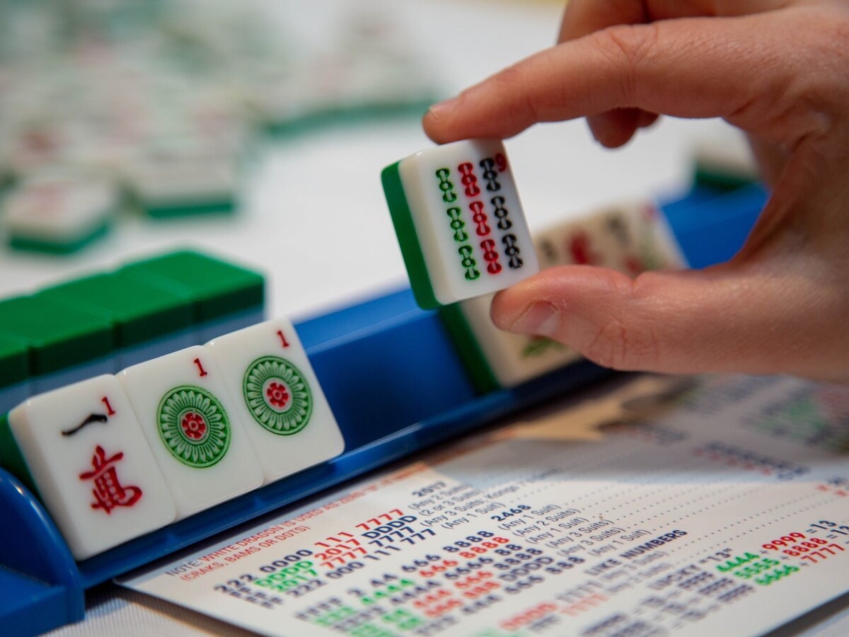 A hand places a mahjong tile during a game.
