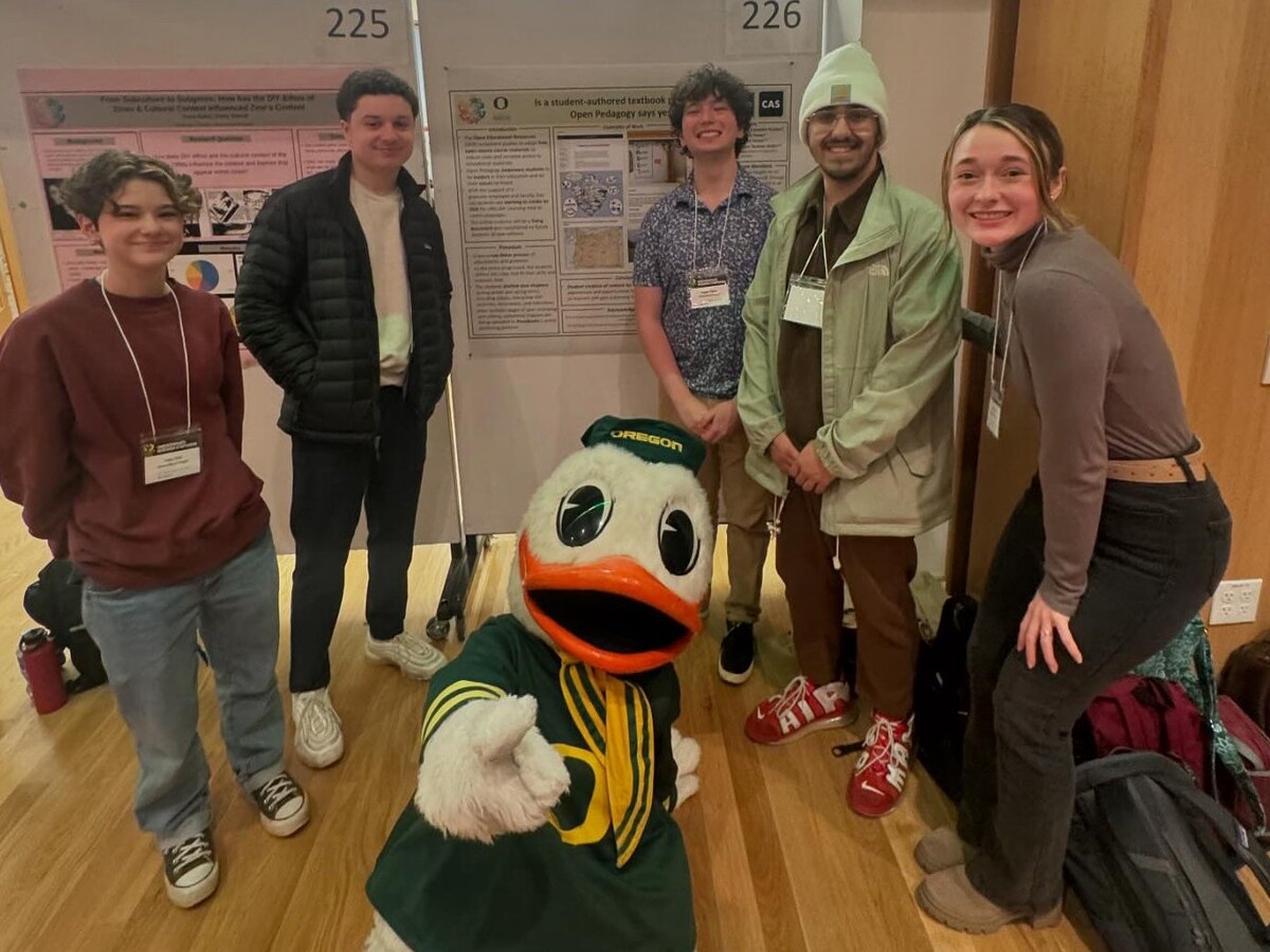 Five people and the Oregon Duck stand by a language textbook poster.
