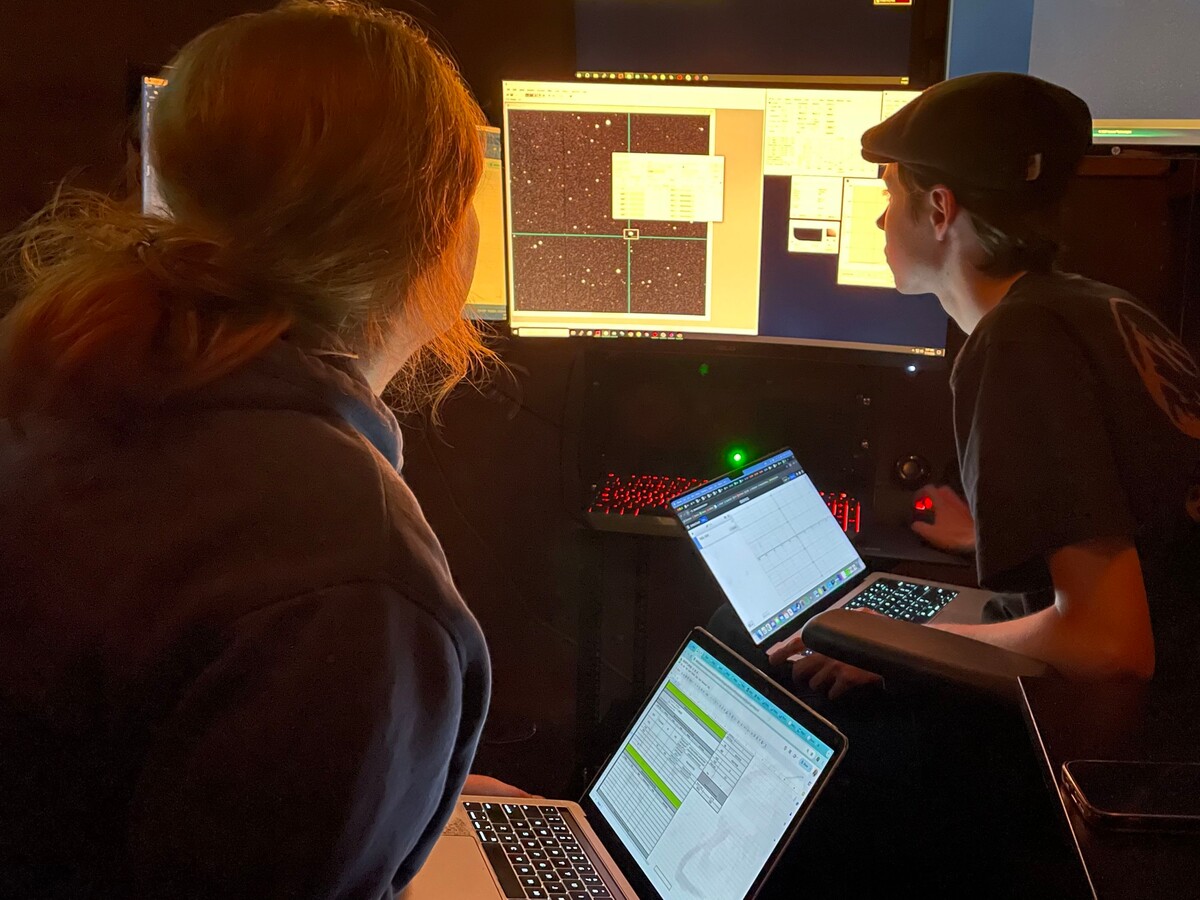 Two researchers review telescope data in a dark control room.