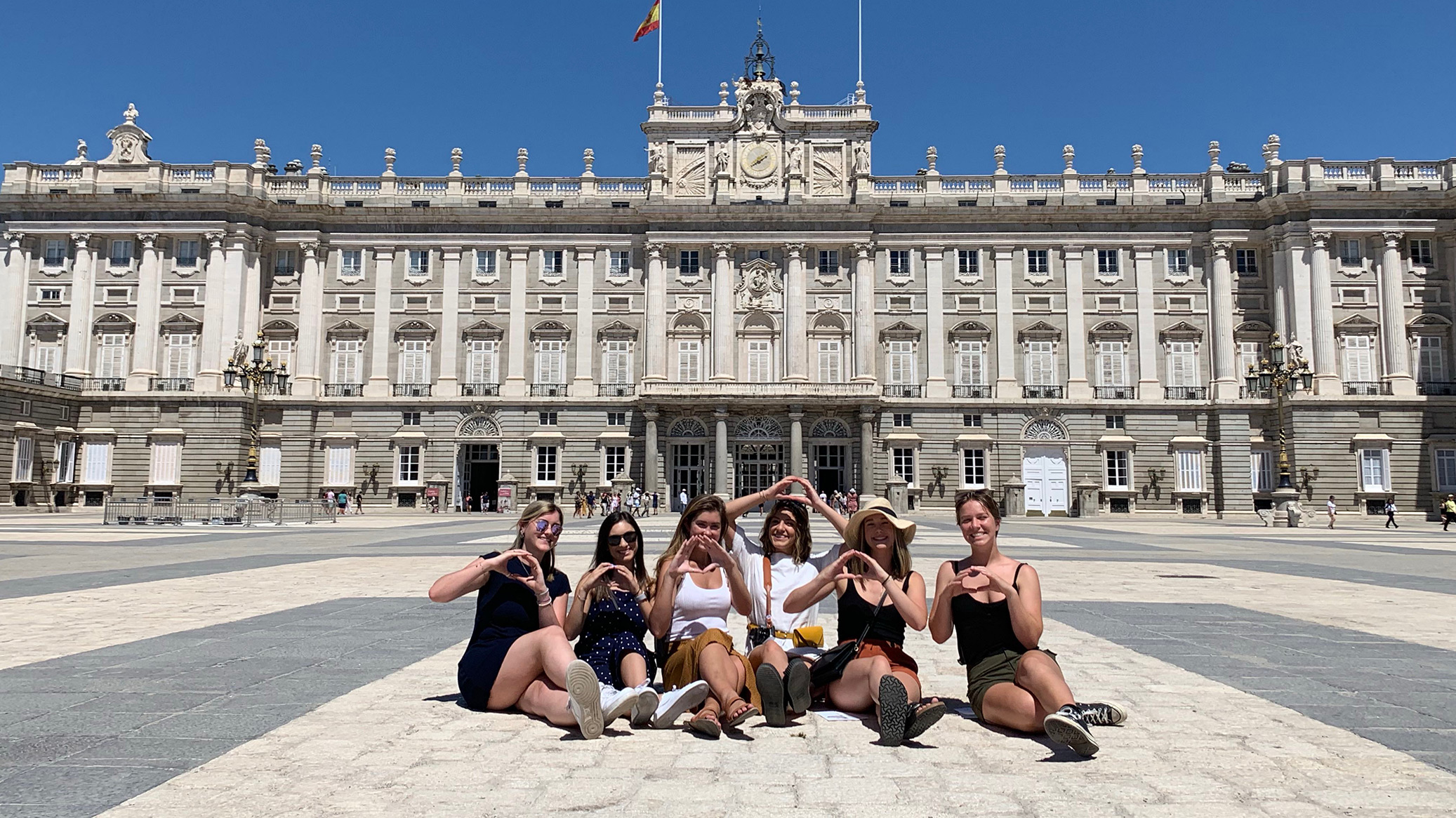 Students sitting in front of a building throwing their O with their hands
