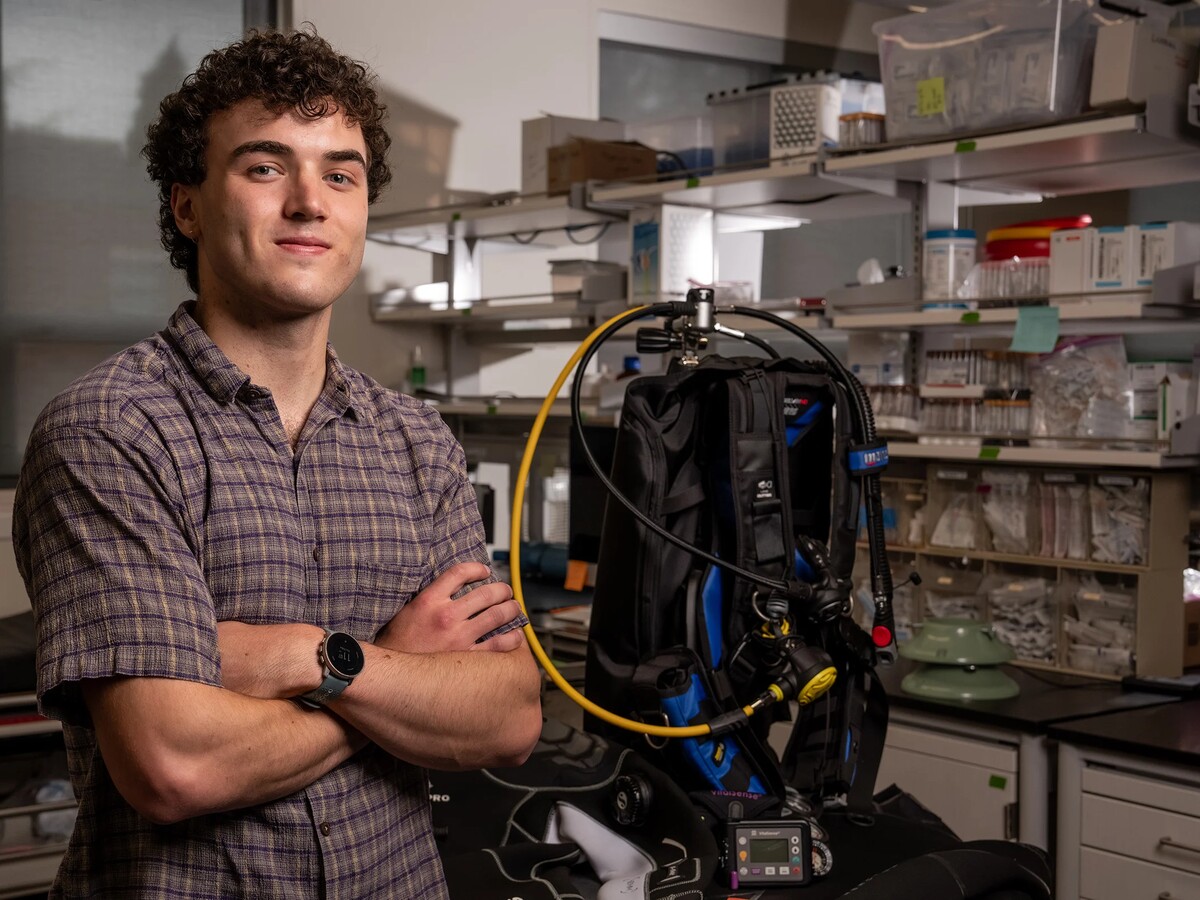 Tucker Orman stands beside scuba research equipment in a laboratory.
