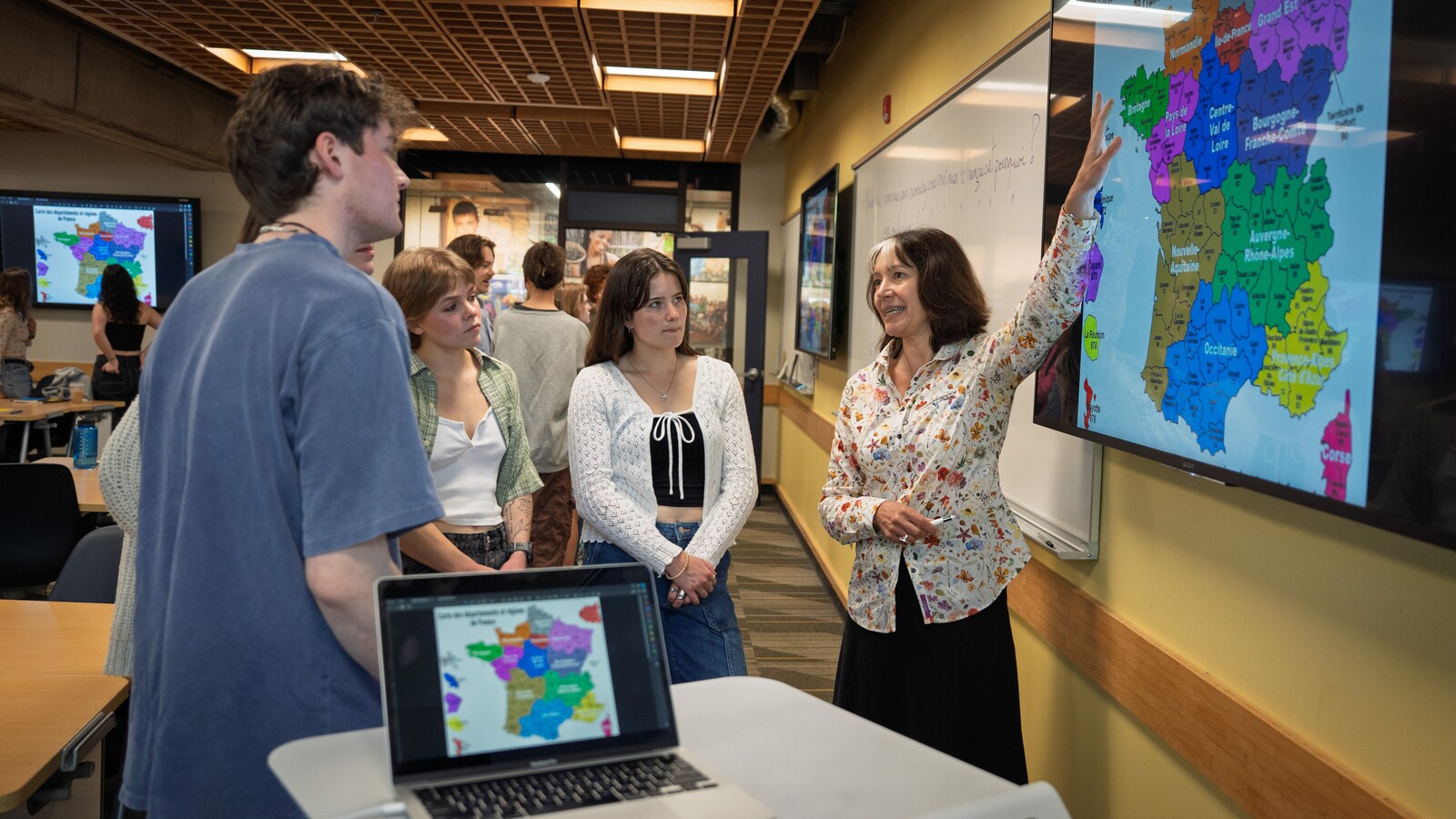 A professor discusses a map of France with students in a classroom.