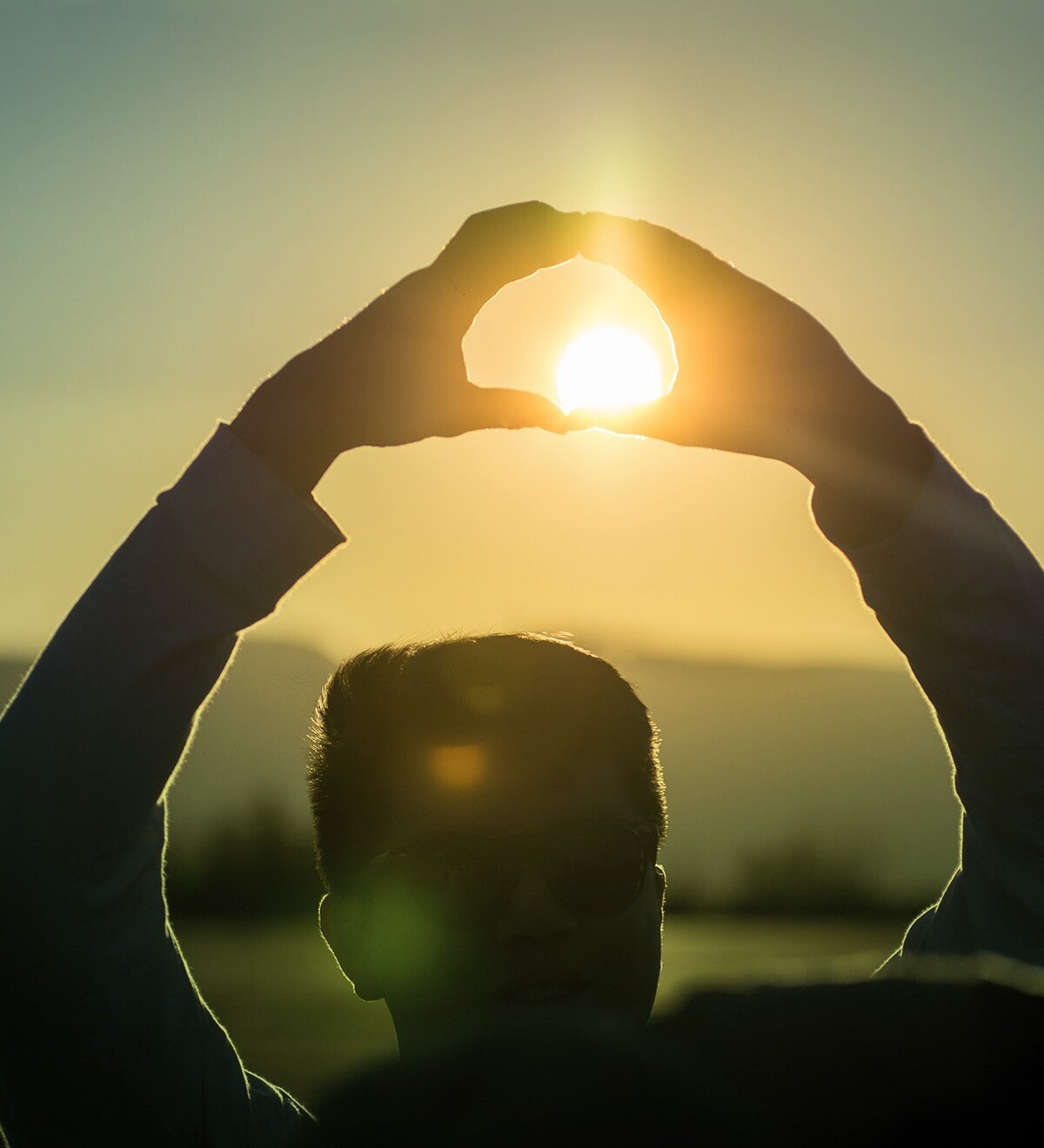 A person frames the setting sun with their hands.