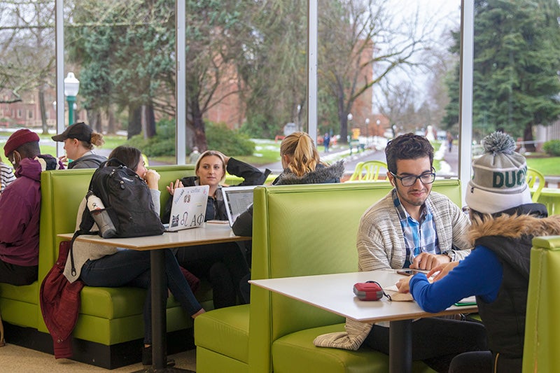 Students sit in green booths in a campus dining hall.