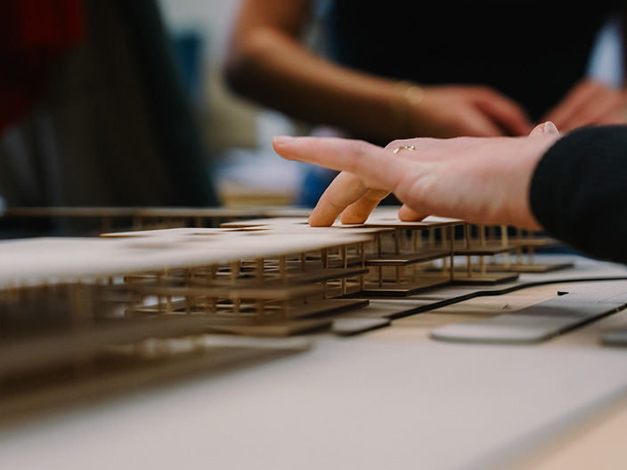 A student's hand touches a model-sized rendition of a design plan for an airport