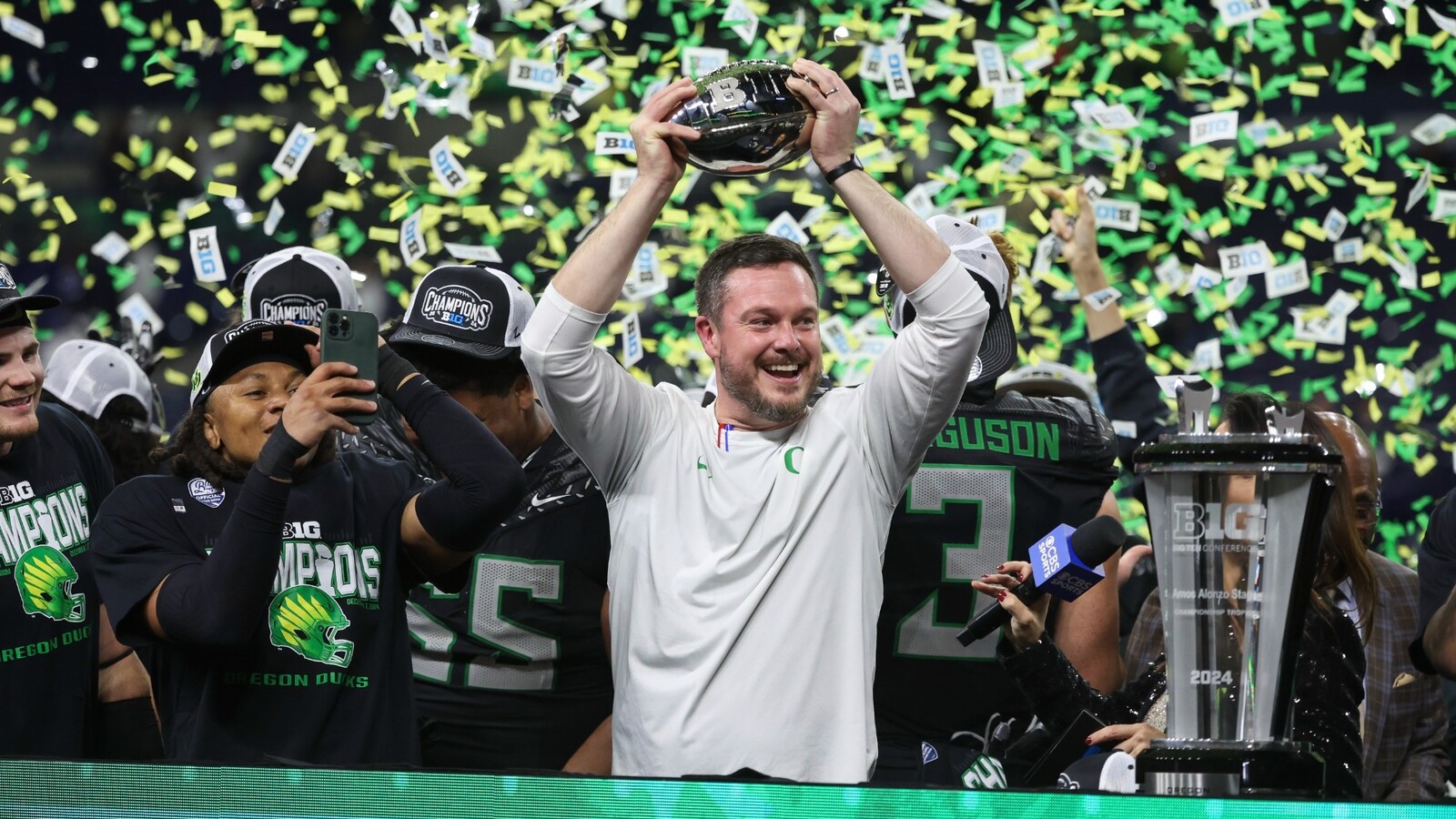 Dan Lanning raises the Big Ten championship trophy amid falling confetti.