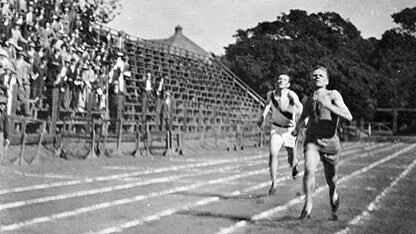 Runners race on an outdoor track as spectators watch.