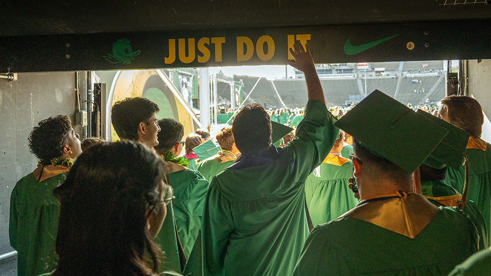 Graduates walking through the tunnel at Autzen Stadium touching the overhead "Just Do It" sign