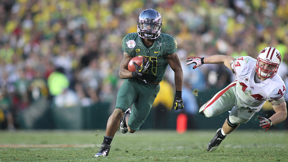 An Oregon football player wearing the green with a chrome helmet runs with a football during a game