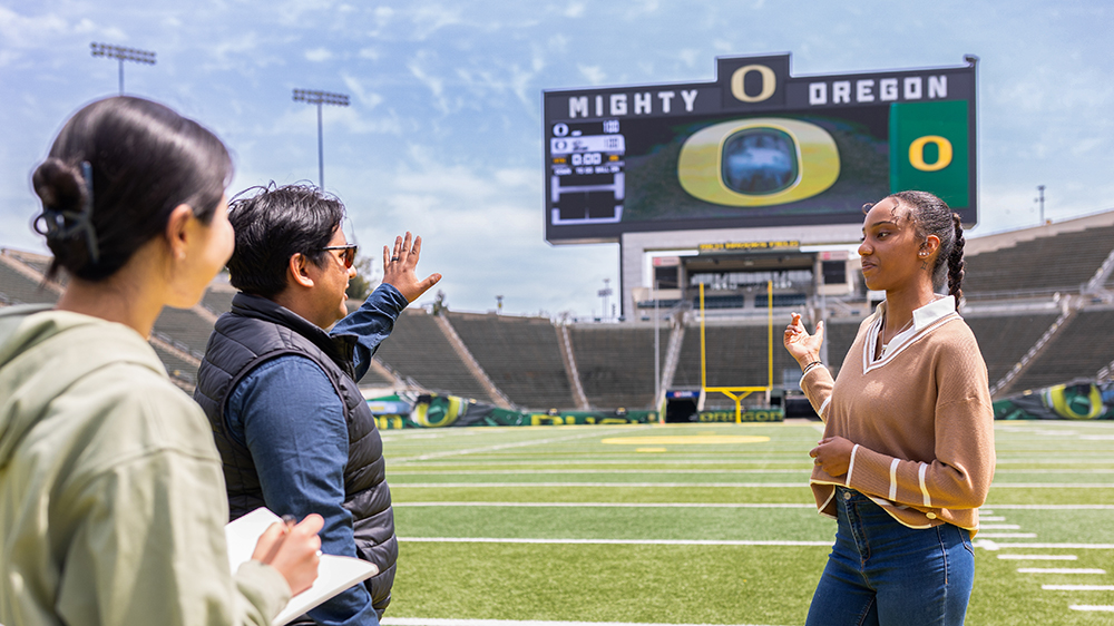 Students and fans standing on the field at Autzen Stadium gesturing to the big screen