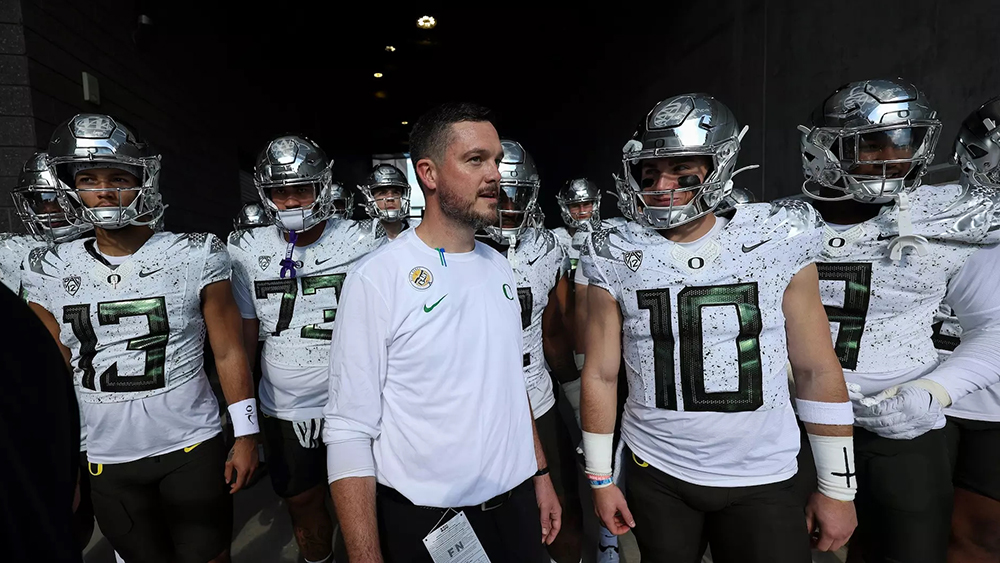 Head coach Dan Lanning standing next to football players wearing the white with speckled jerseys in an Autzen stadium tunnel.