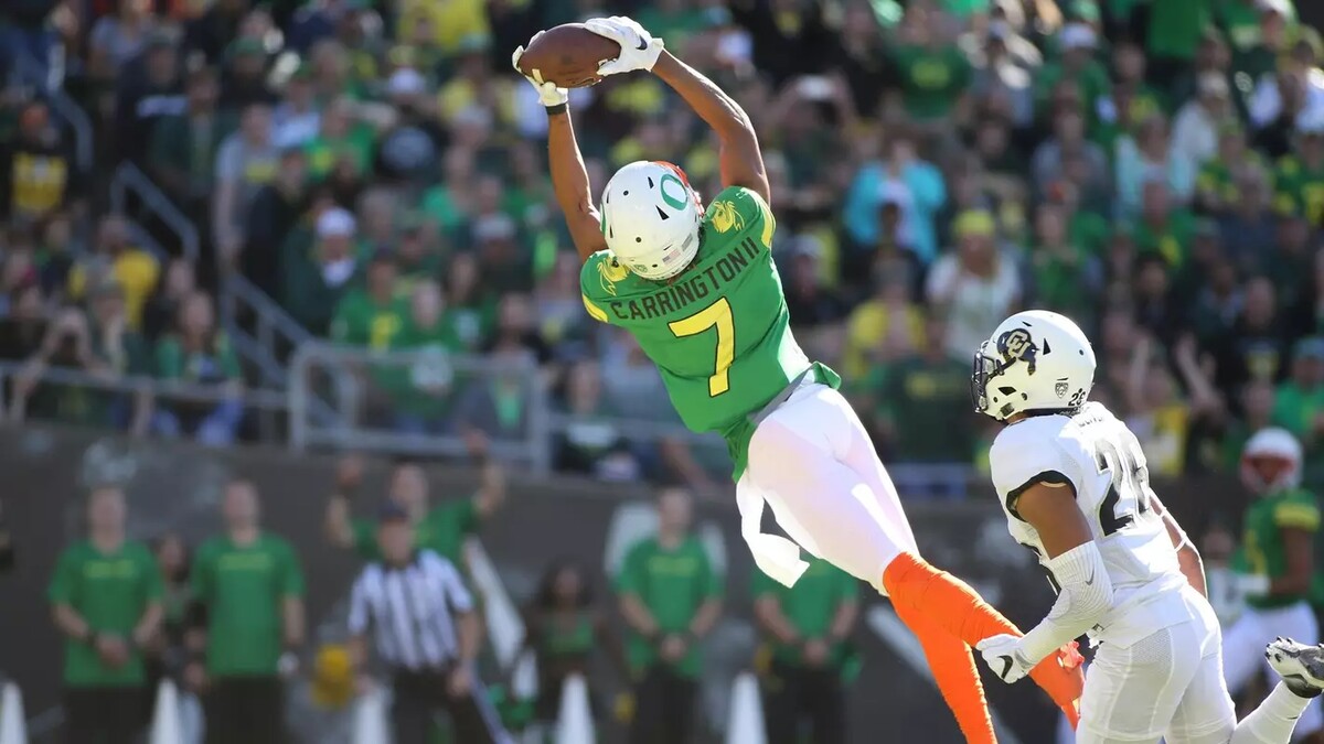 An Oregon football player catches a ball during a game in a uniform matching The Ducks mascot.