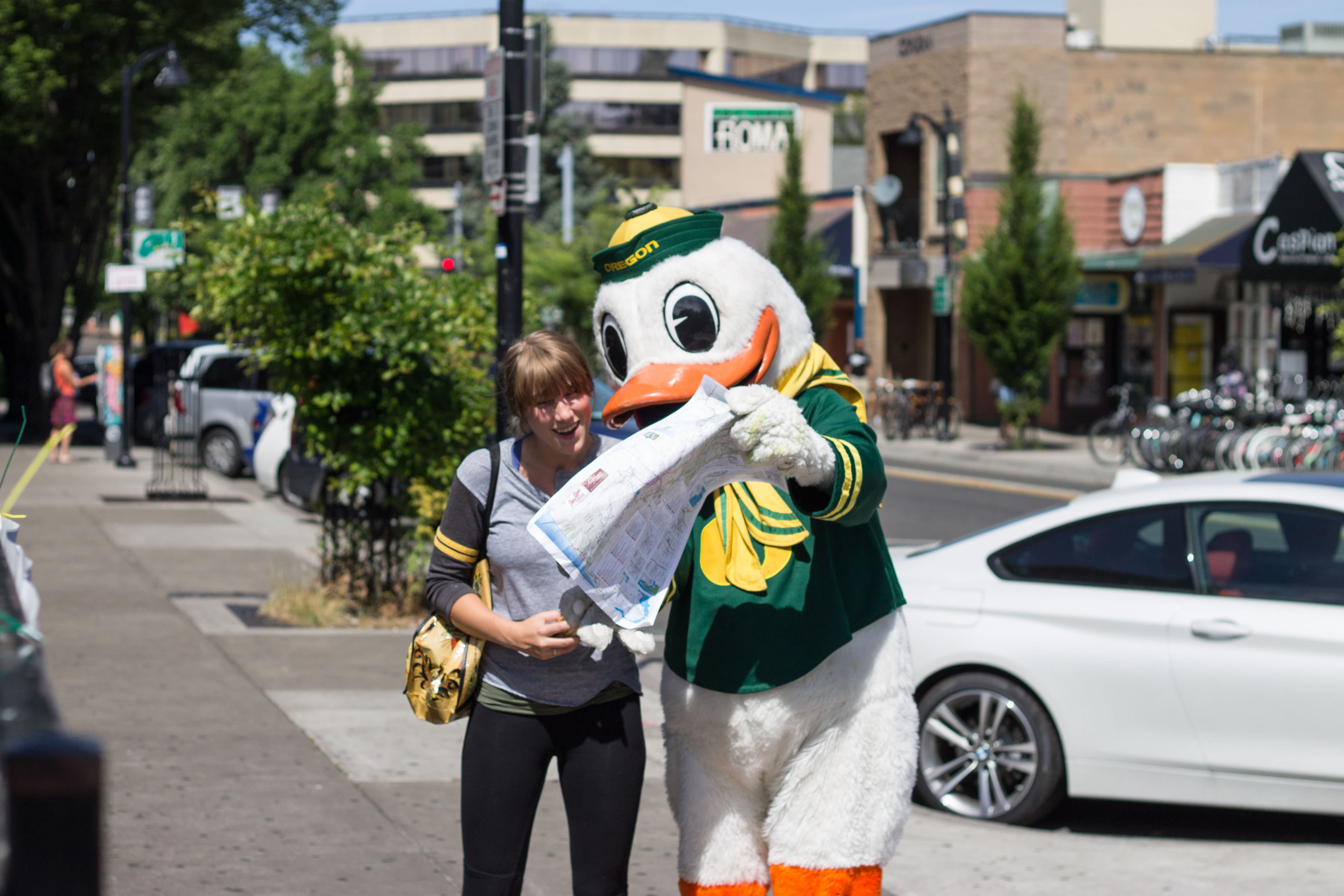 The Oregon Duck holding a map with a visitor on a sidewalk.
