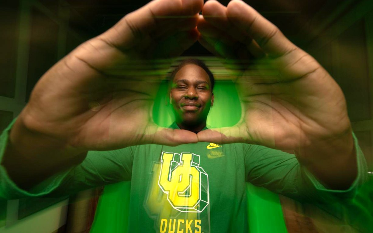 A person forms an O with their hands while wearing an Oregon Ducks shirt.