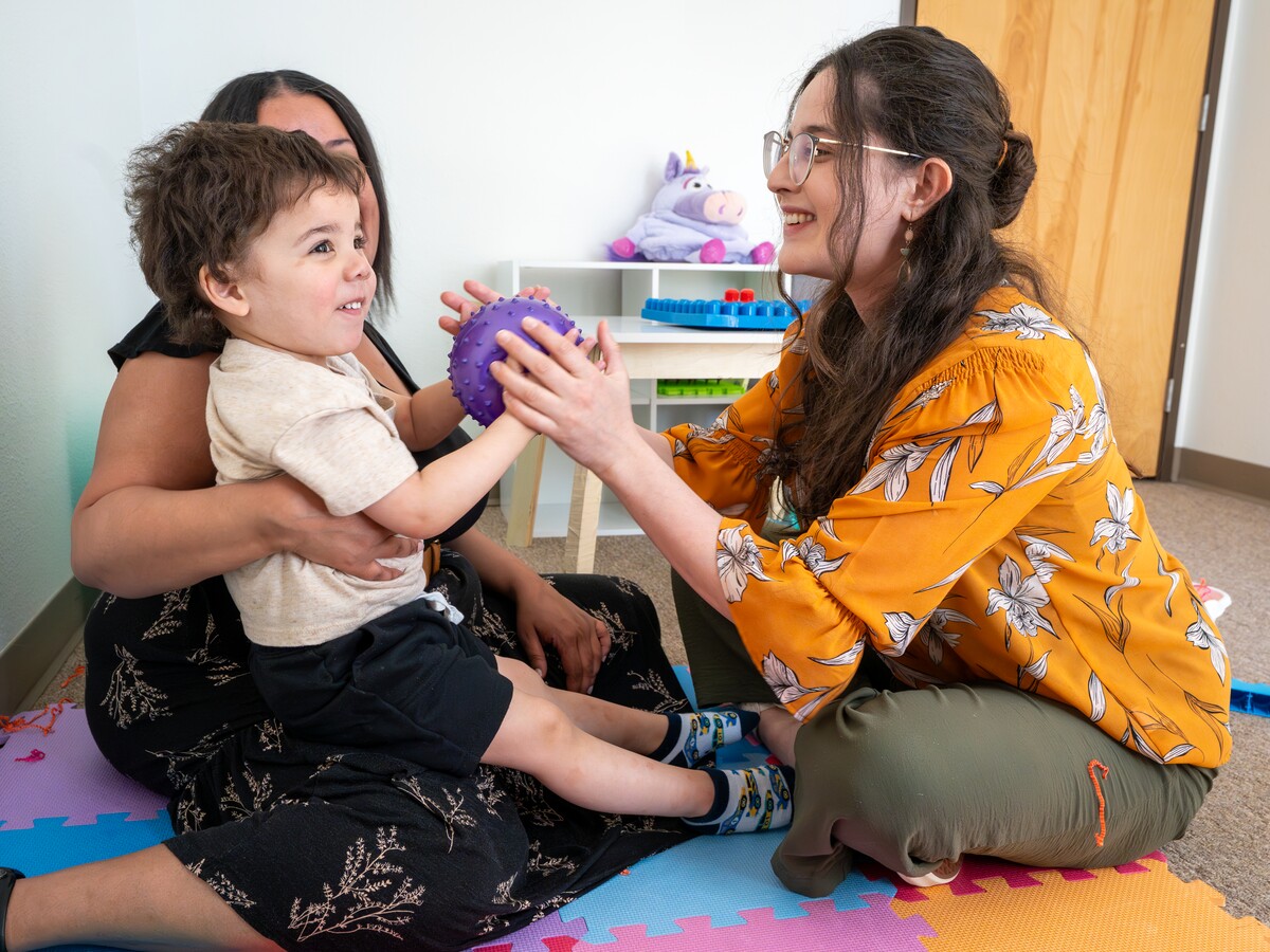 An adult and child play with a purple ball.