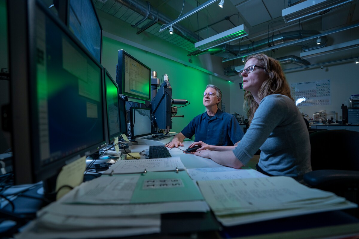 Two researchers review data beside specialized laboratory equipment.