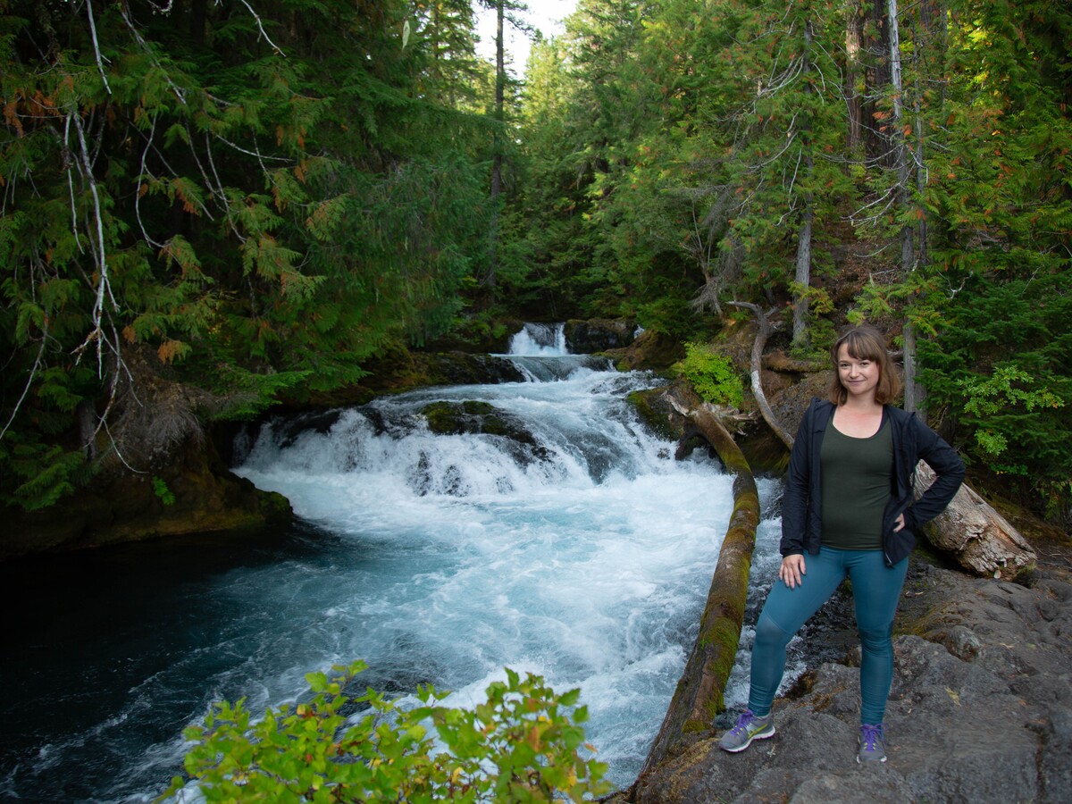 A visitor stands beside a rushing forest waterfall.