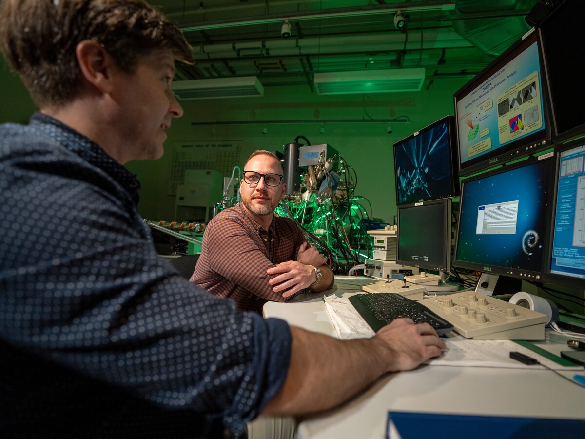Two researchers discuss data on laboratory monitors.