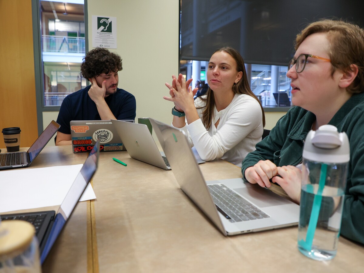 Three people talk around a table of laptops.