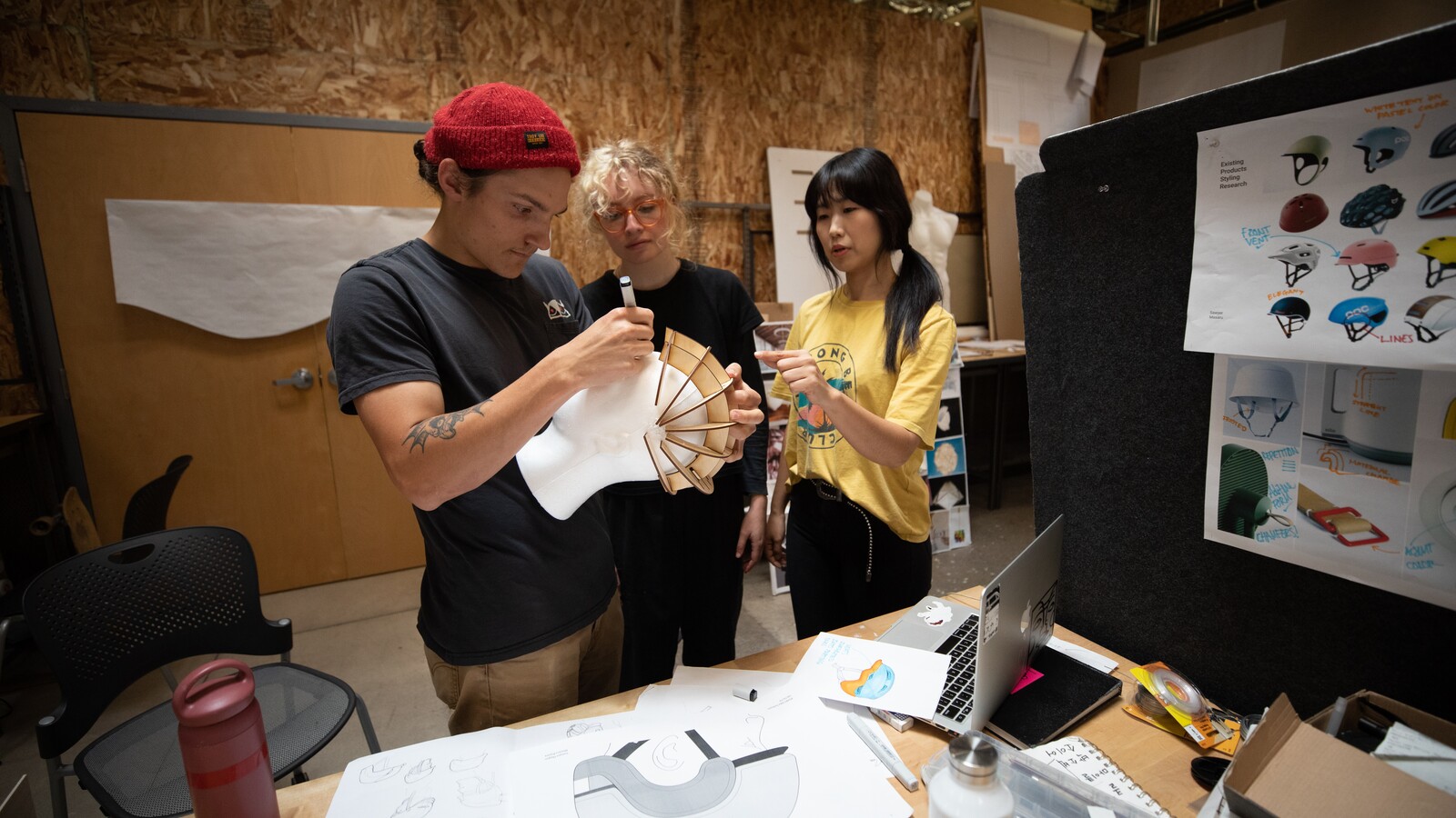 Three people examine a helmet prototype in a product-design studio.