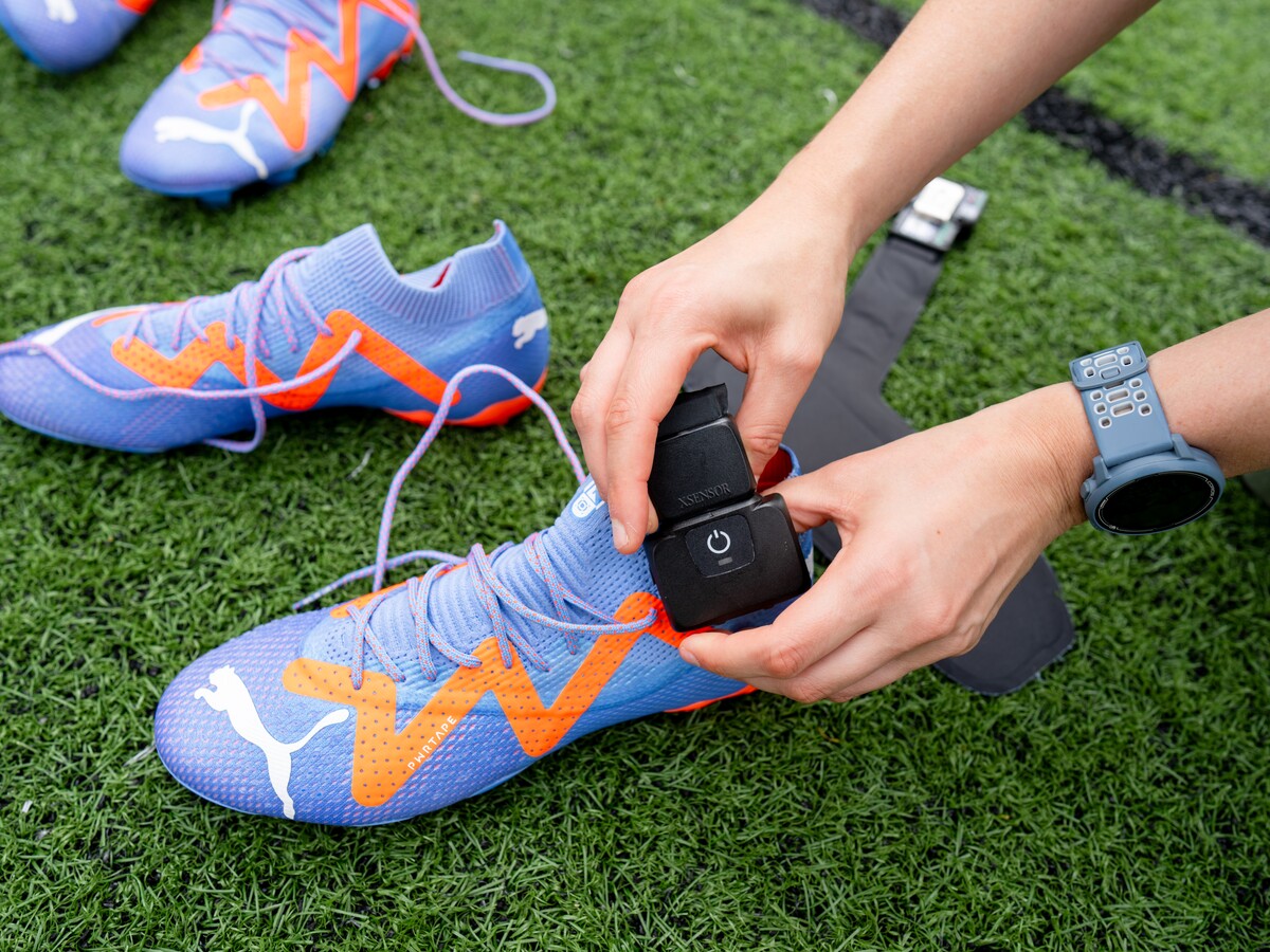 Hands attach a sensor to a Puma soccer cleat on turf.