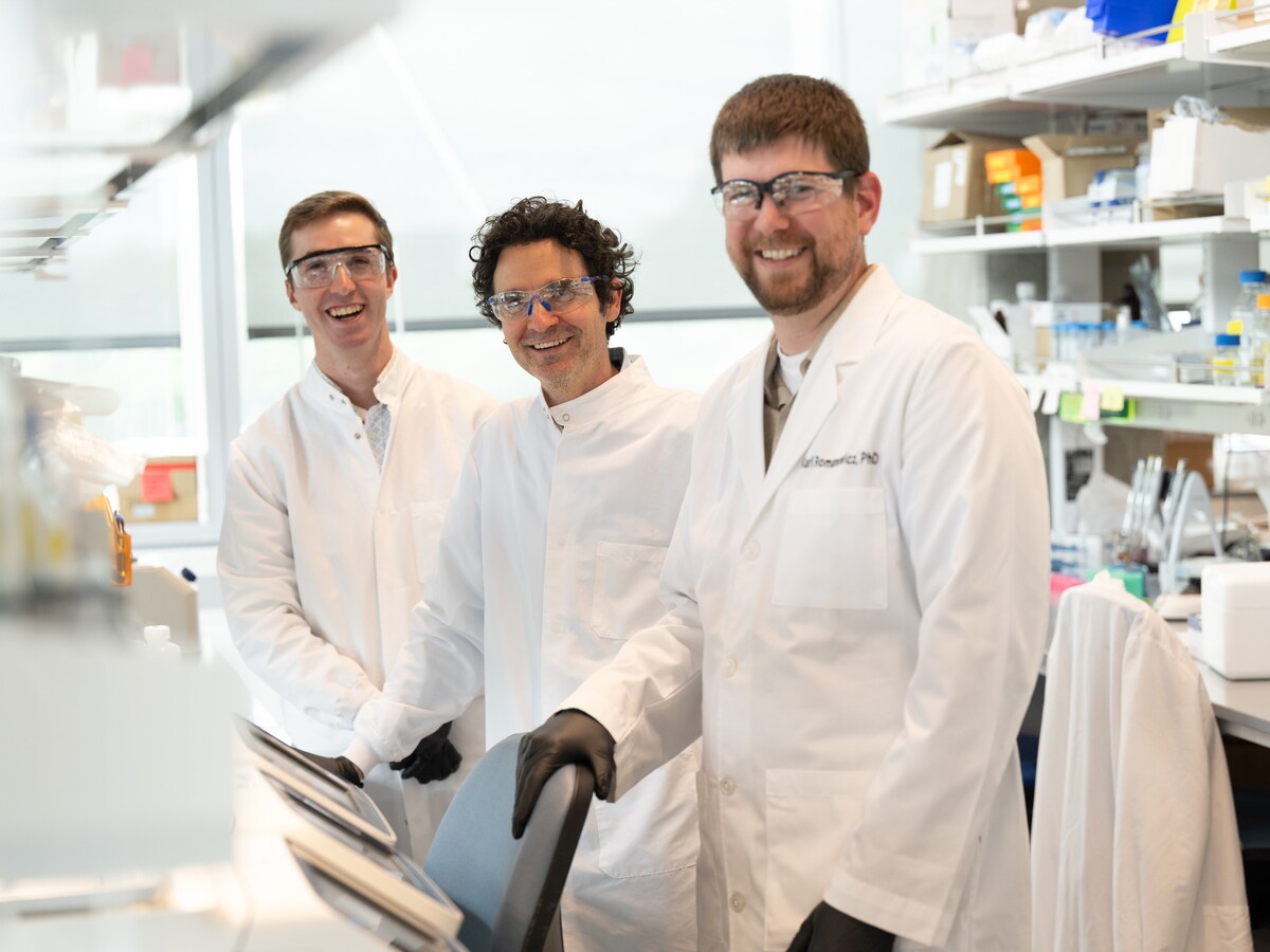 Three researchers stand together in a laboratory.
