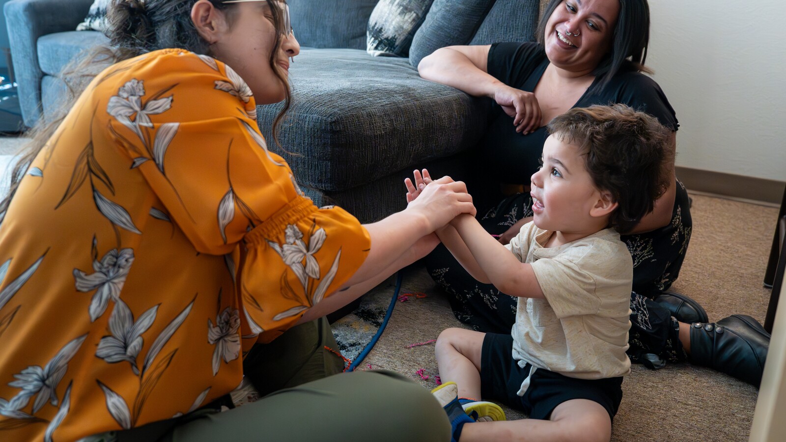 A researcher plays with a child while a family member watches.