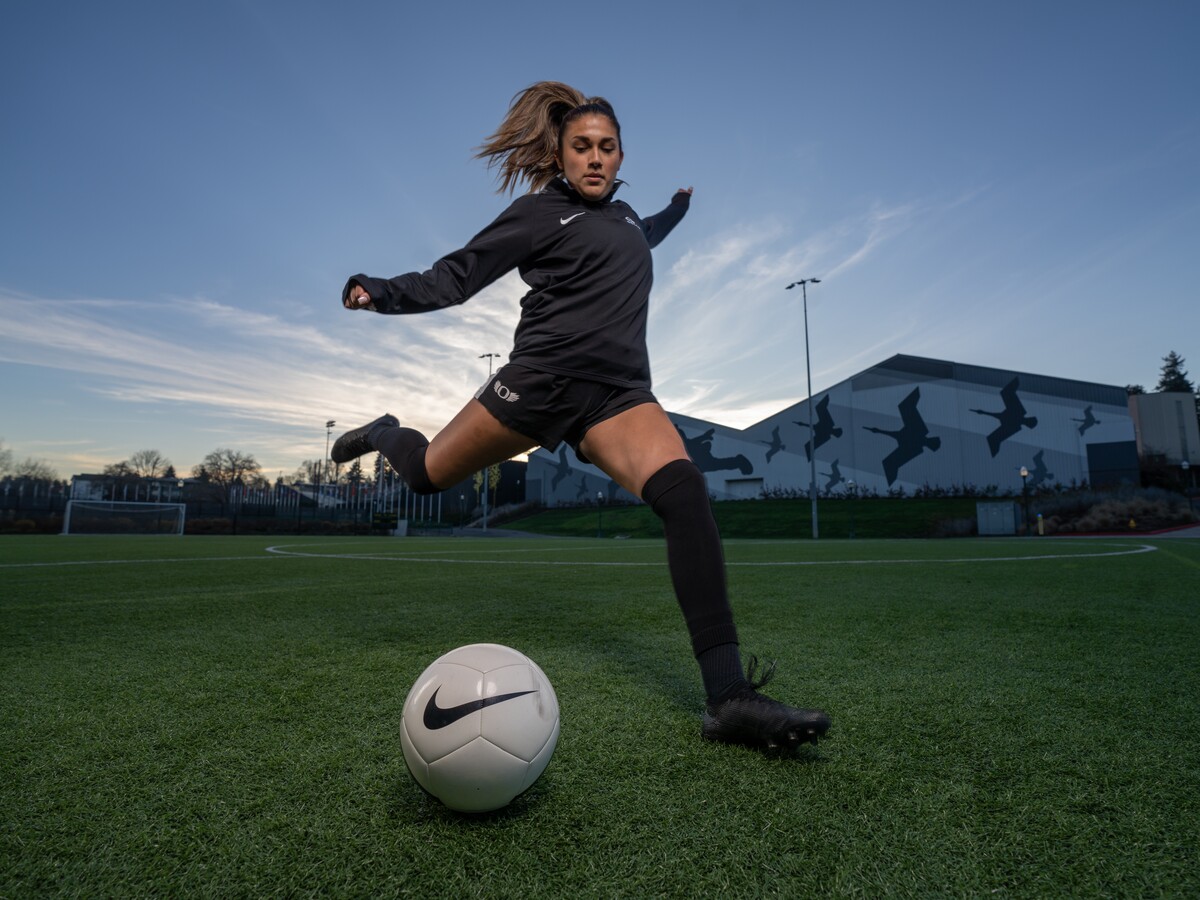 An athlete kicks a soccer ball on an outdoor field.