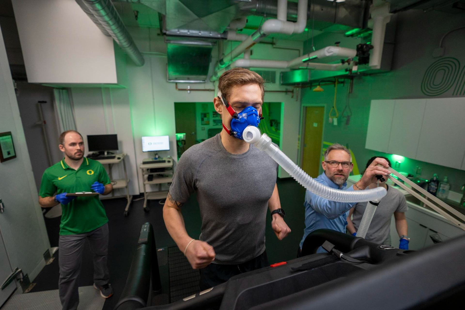 A researcher monitors an athlete wearing exercise testing equipment.