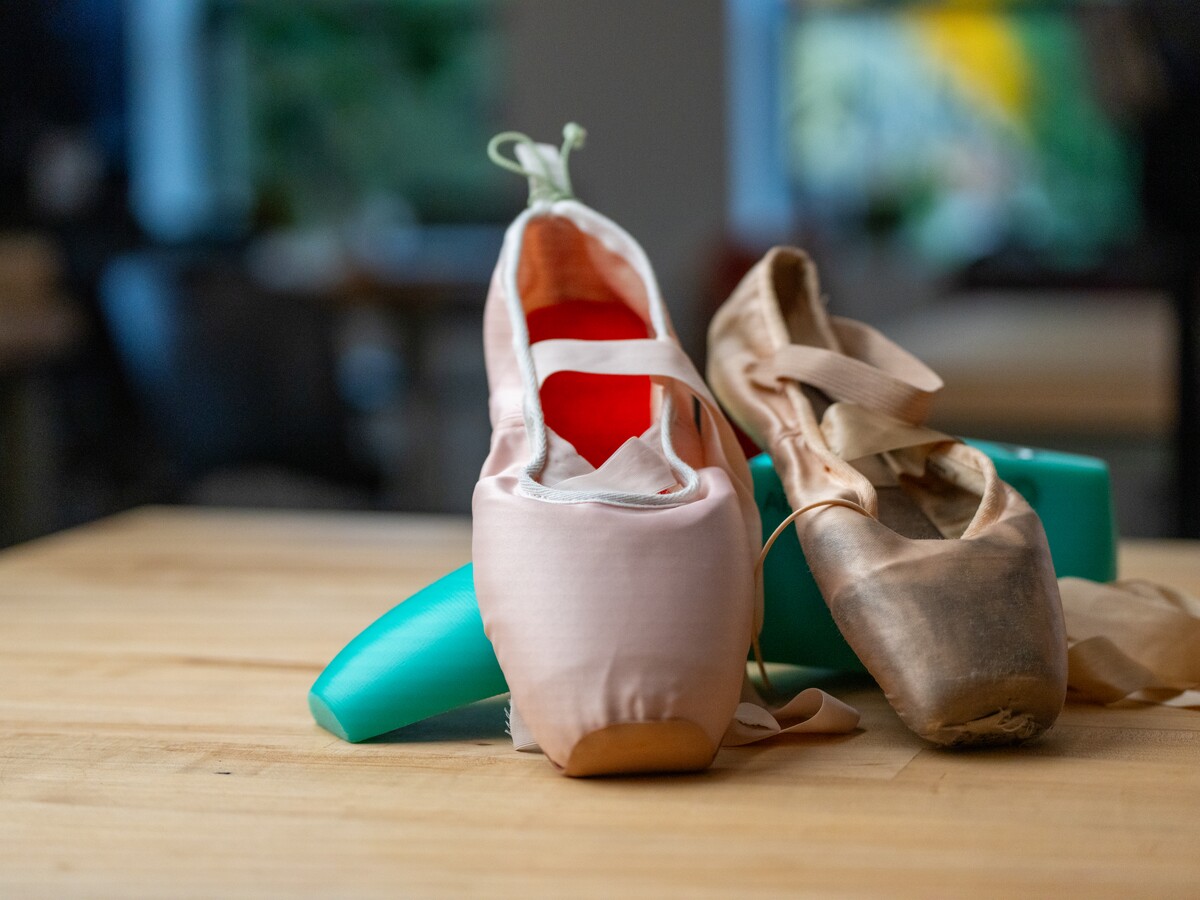 A prototype ballet shoe stands beside a worn pointe shoe.